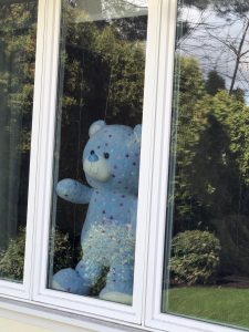 Blue stuffed animal bear with hearts standing in window looking outside